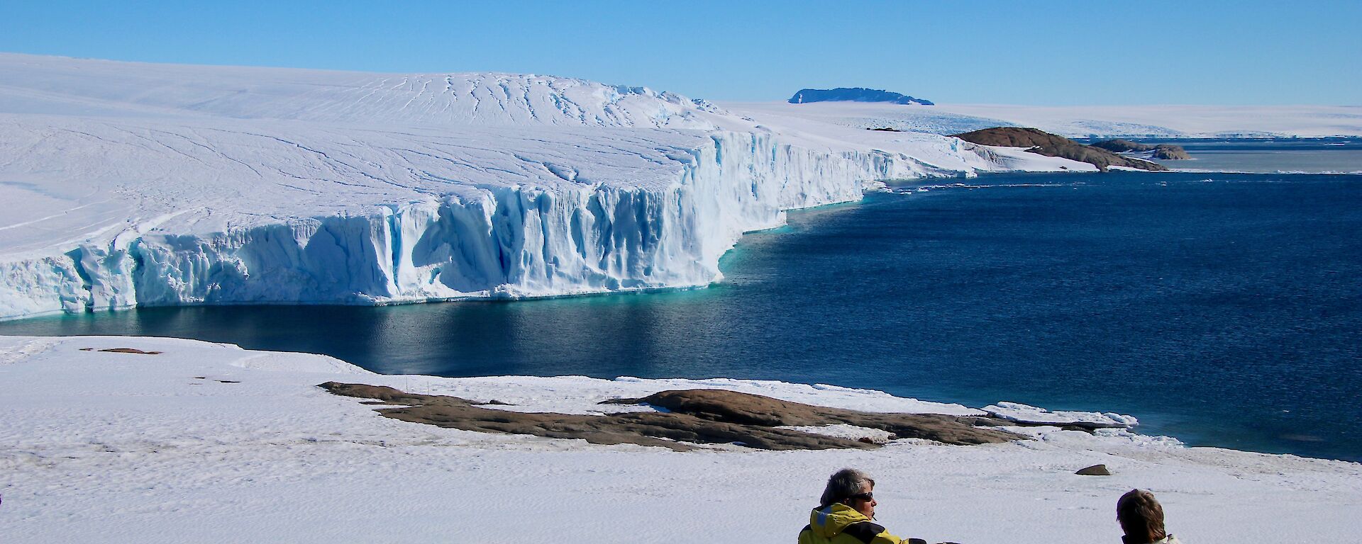 Arts Fellows Jesse and Jane sitting on rocks looking over the ocean and out to an ice cliff in the distance.