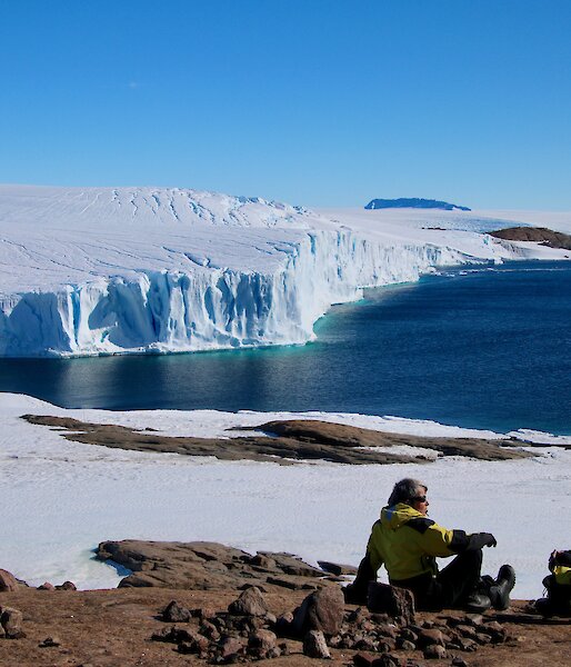 Arts Fellows Jesse and Jane sitting on rocks looking over the ocean and out to an ice cliff in the distance.