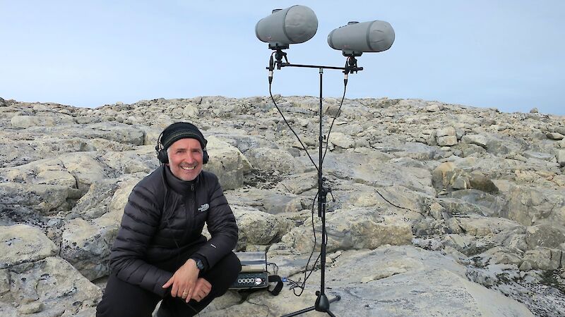 Sound artist with microphone on stand in the field with station in background