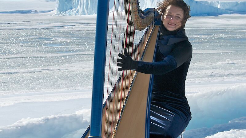 Harpist playing harp on ice with ice cliffs in background