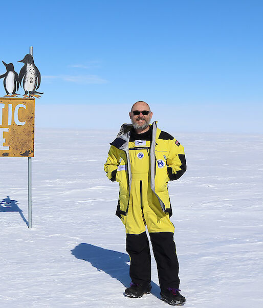 An expeditioner stands next to a sign that says "Antarctic Circle".