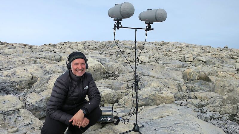 An expeditioner in the field stands next to 2 large microphones.
