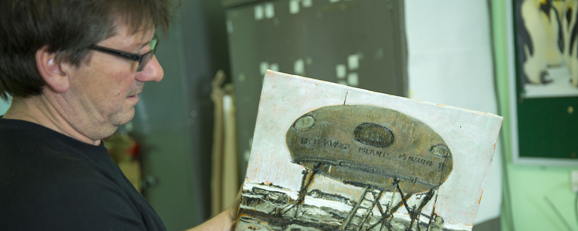 Artist John Kelly holding artwork depicting a Googie field hut.