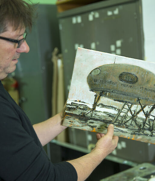Artist John Kelly holding artwork depicting a Googie field hut.