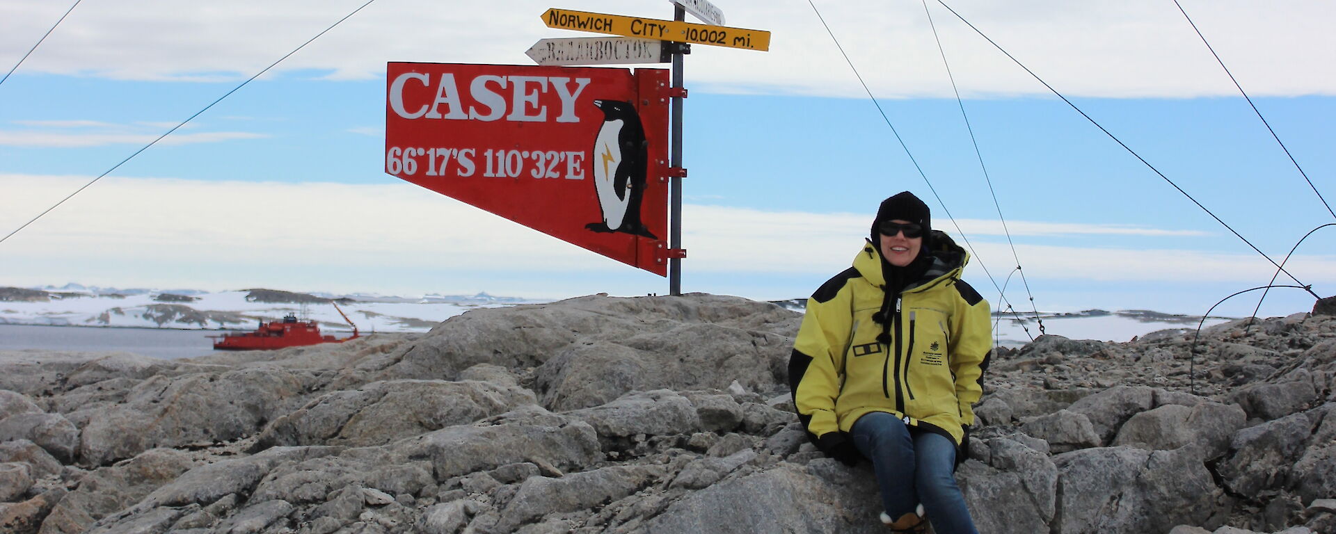 An expeditioner sits in an icy landscape next to a sign that says "Casey".