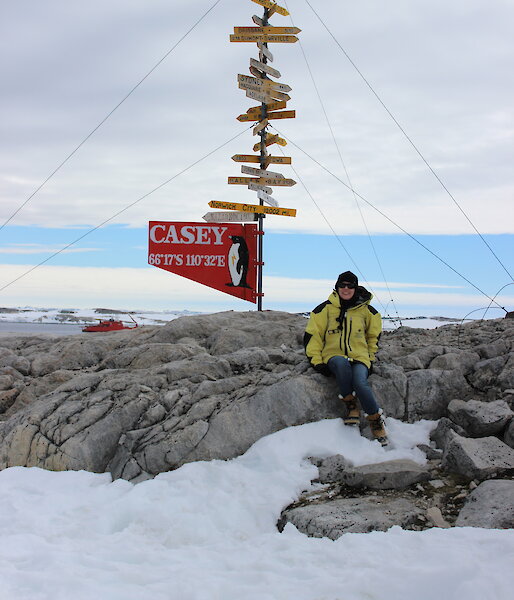 An expeditioner sits in an icy landscape next to a sign that says "Casey".