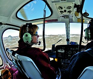 2 expeditioners in a helicopter look out over a vast landscape.