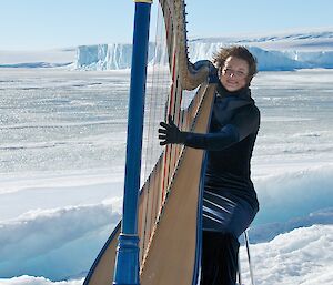 Harpist playing harp on ice with ice cliffs in background