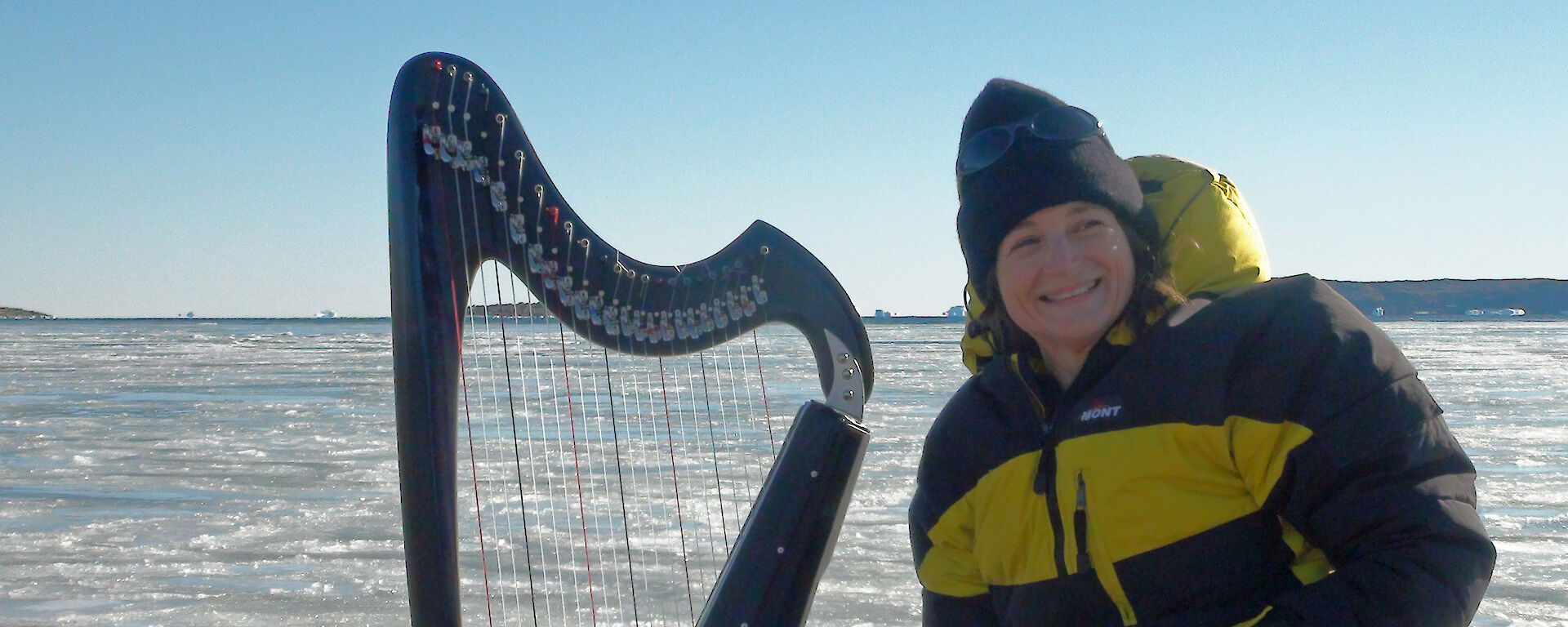 A musician sits with a harp at the edge of an icy bay.