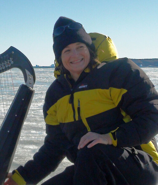 A musician sits with a harp at the edge of an icy bay.