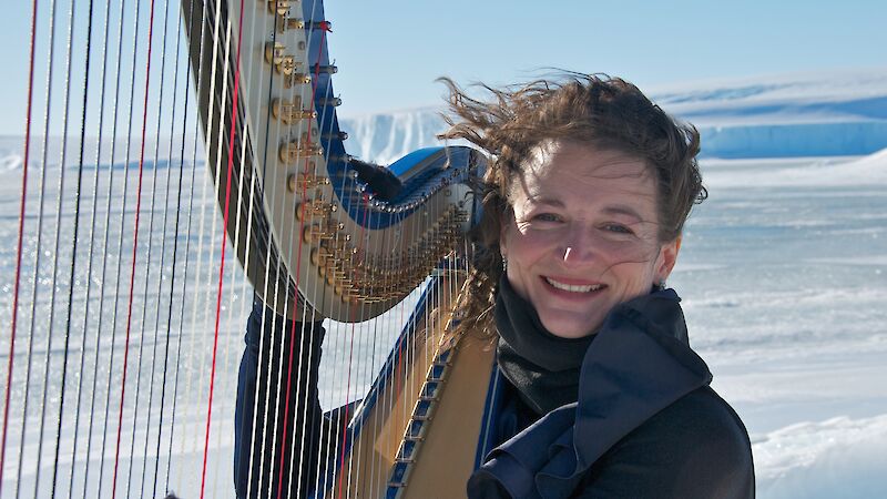 A musician with her harp in an icy landscape. The wind catches her hair.