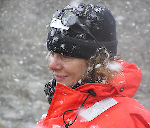 An expeditioner dressed in red stands in the falling snow.