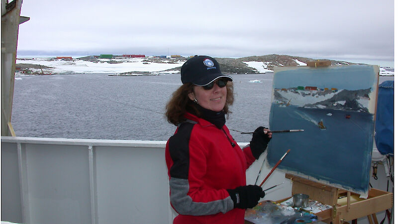 Artist painting at easel on the deck of the ship with station in background