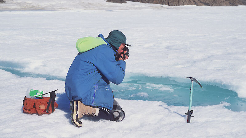 Denis Crawford kneels on the ice and takes photos.