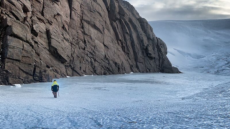 An expeditioner standing on the ice at the base of a mountain