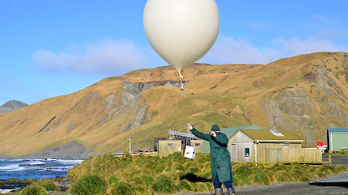Expeditioner releasing meteorological balloon on clear day.