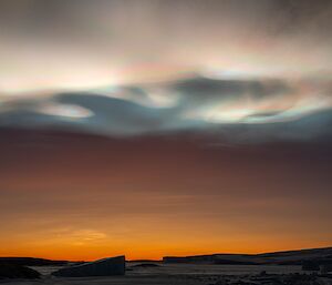 Iridescent clouds above an orange sunset over icebergs