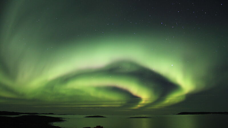 Green Aurora Australis over water and shoreline.