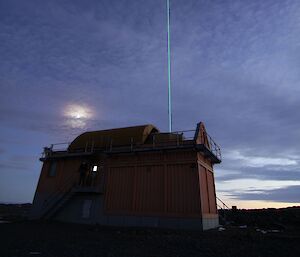 A thin laser beam shoots from the top of a small shed