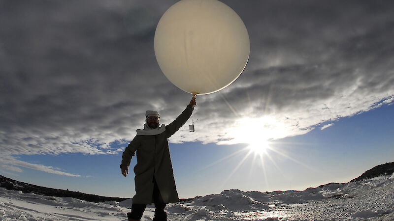Low angle view of meteorologist launching meteorological balloon, with dark clouds over head. Sun rays at edge of dark cloud cover