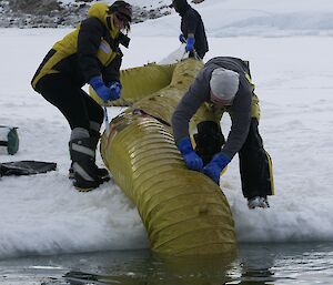 A large yellow tube is lowered into the water by 3 expeditioners.