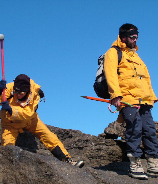 Geologist wielding pick axe, other standing nearby