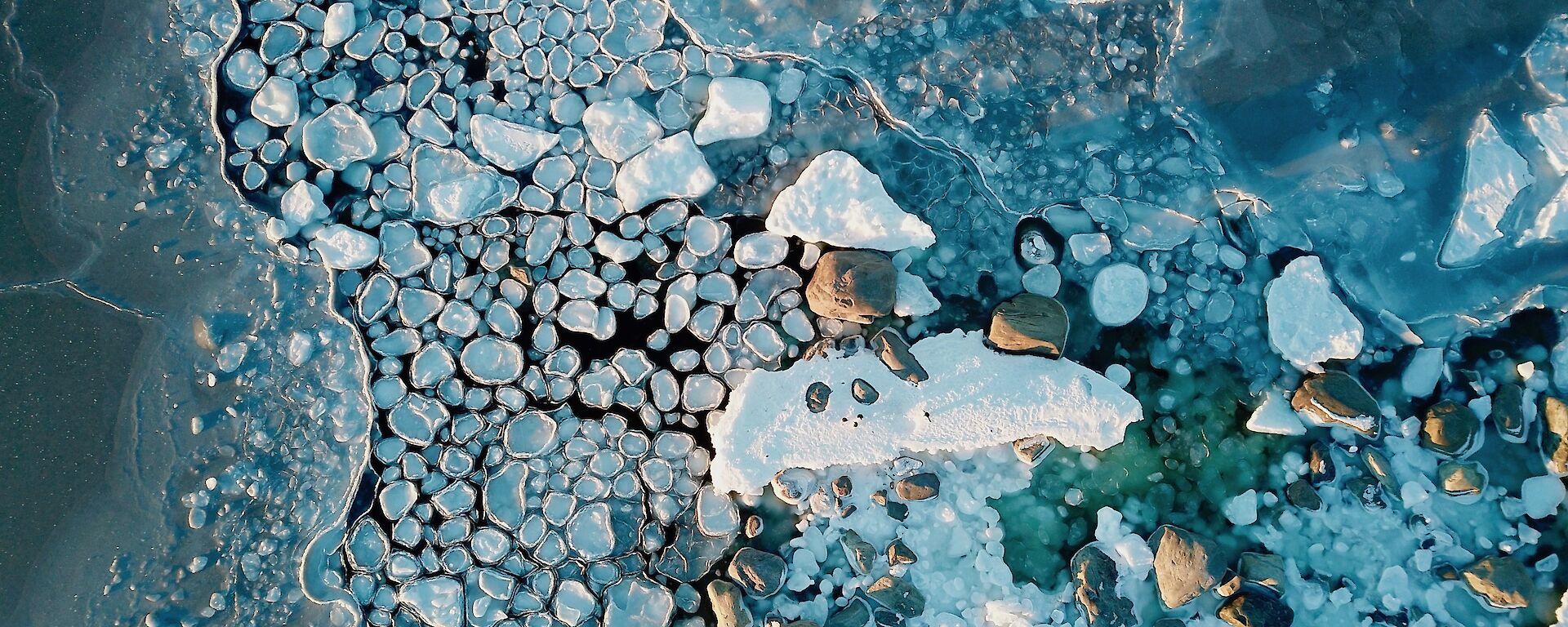 Photo taken from a drone, a shot taken from above looking down at the edge of the water as the ice forms and the wind action creates rounds of ice that look like lilypads
