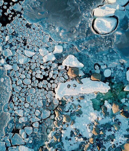 Photo taken from a drone, a shot taken from above looking down at the edge of the water as the ice forms and the wind action creates rounds of ice that look like lilypads