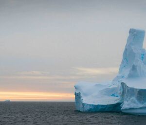 Detail of pinnacled iceberg with pink glow of evening light over horizon.