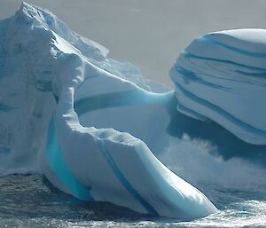 Striped blue iceberg being weathered by waves