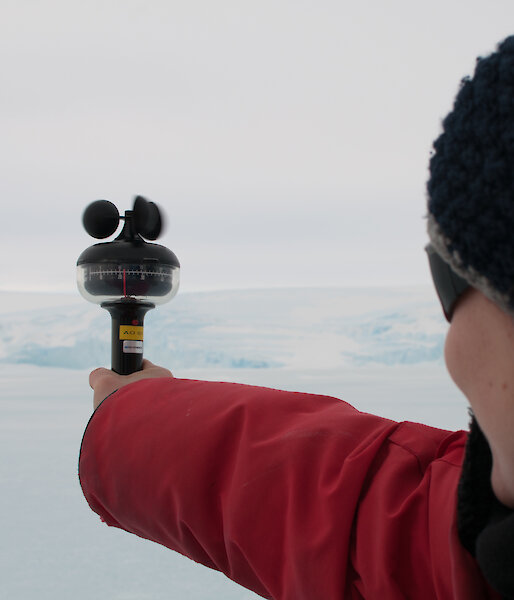 Expeditioner holding instrument at arm’s length to measure wind speed and direction
