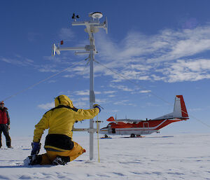 Expeditioner kneels to inspect the AWS with aircraft in the background.