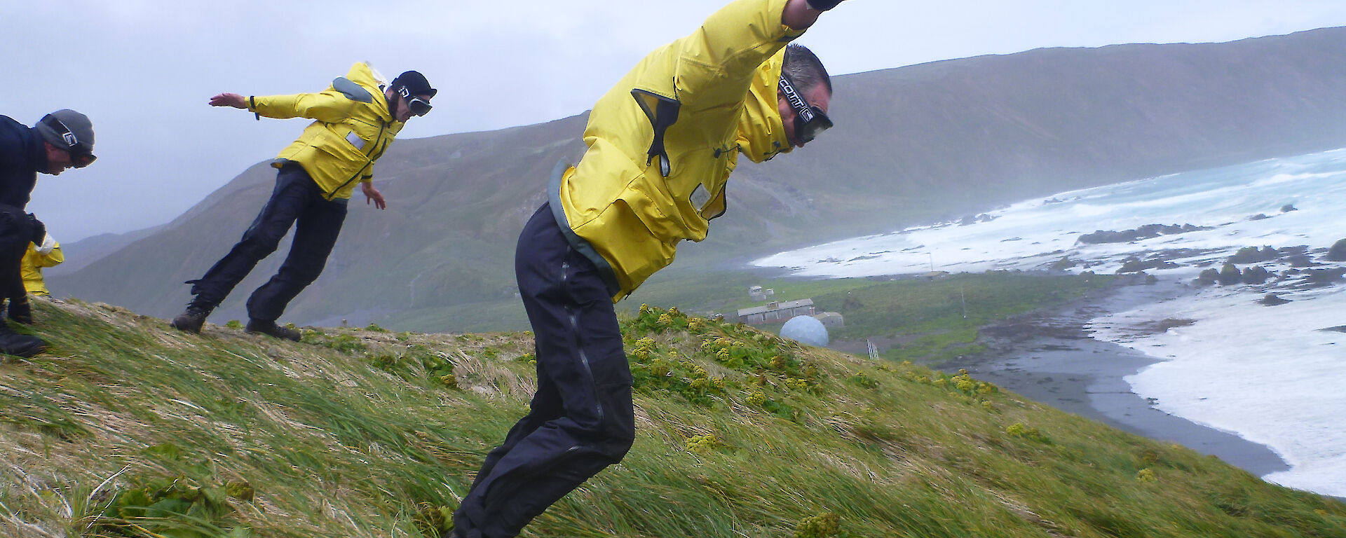 Two yellow clad expeditioners leaning on the wind atop hill