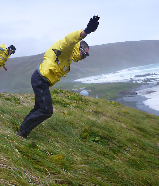 Two yellow clad expeditioners leaning on the wind atop hill