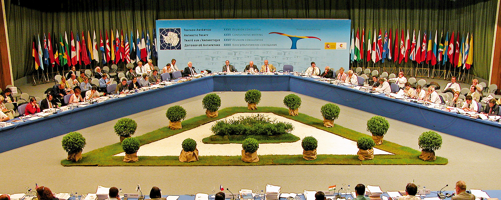 Members of Treaty Parties meeting in a large building decorated with Treaty countries’ flags.