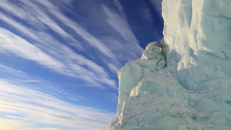 A blue-tinted iceberg in front of a bright blue sky.