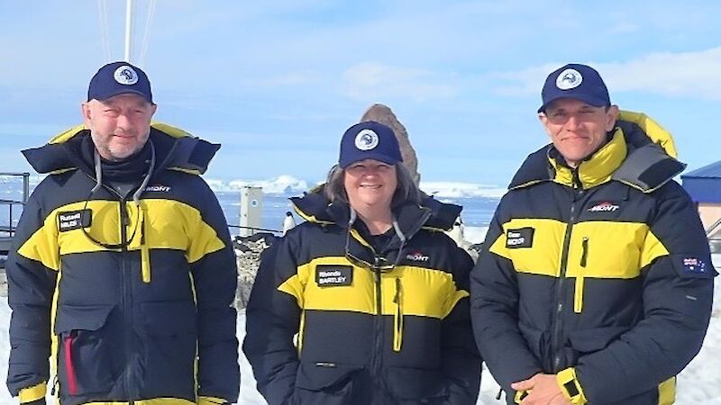 Three people wearing cold weather clothing standing in front of a flagpole with the French and Australian flags.