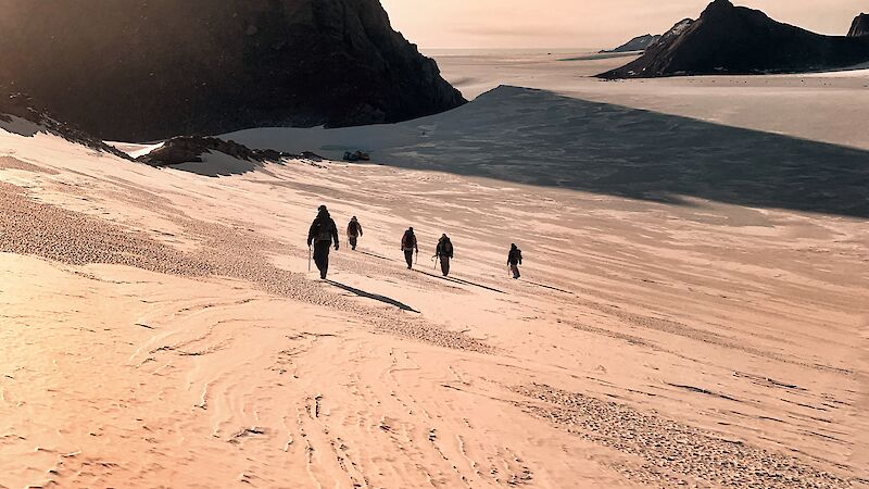 Sun above mountain peak with a group of expeditioners walking below