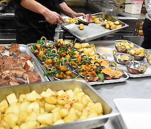 Chef behind large kitchen bench which is laden with food