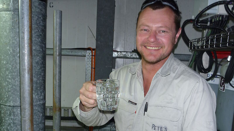A plumber holding a glass of fresh water in a plant room.
