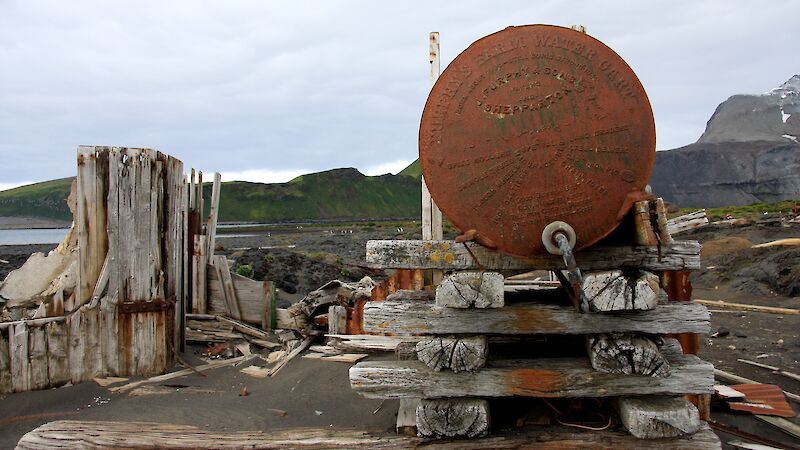 Rusted tank on wooden stand along coastline