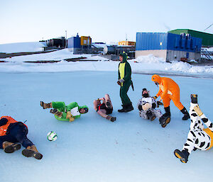 Expeditioners playing soccer on the fast ice with players dressed in onesies rolling on the ice.