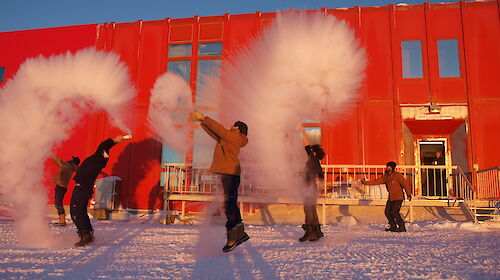 A team of expeditioners throwing boiling water from jugs into the cold air