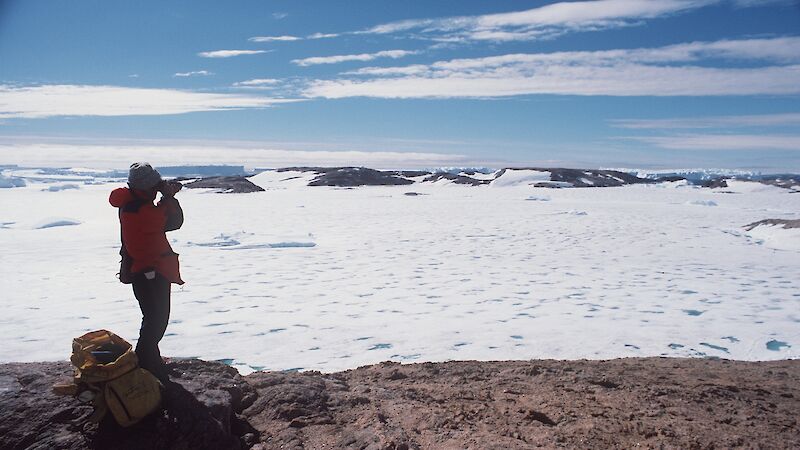 Expeditioner standing on a rocky hill taking a photo of an icy landscape