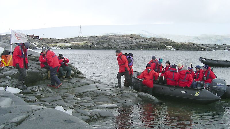 Inflatable boat at the shore as tourists in red life jackets disembark.