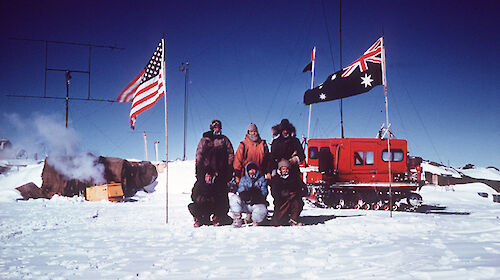 The traverse party stand in front of the vehicle and flags at Vostok
