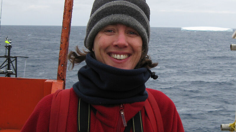 Wendy standing on the deck of the Aurora Australis with an iceberg in the distance