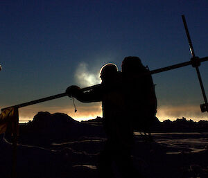 Silhouette of scientist carrying a large cross across the sea ice