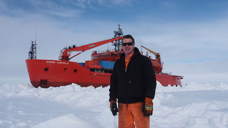 Man standing on ice beside ship