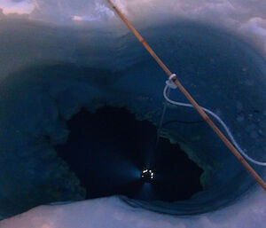 Hole in the ice with light from the krill trap shining up from the icy dark depths